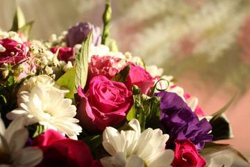 A bouquet of pink roses, lilac flowers of Alstroemeria and white small chrysanthemums, standing near the window and lit by the sun's rays