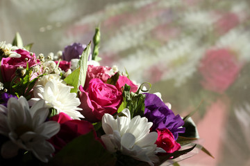 A bouquet of pink roses, lilac flowers of Alstroemeria and white small chrysanthemums, standing near the window and lit by the sun's rays