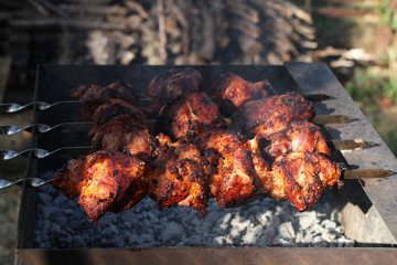 Pork barbecue shashlik on skewers frying on a grill brazier against fire wood stack and green grass background