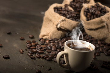 Coffee cup and sacks with coffee beans on a black table.
