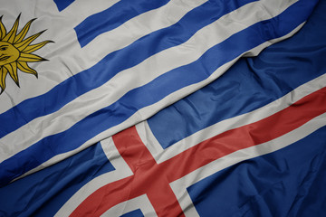 waving colorful flag of iceland and national flag of uruguay.