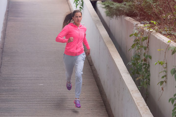 Young female runner in hoody is jogging in the city street.Fit body requires hard work. Urban sport concept. Young female exercising in sport clothes.