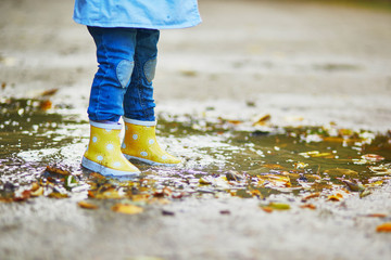 Child wearing yellow rain boots and jumping in puddle