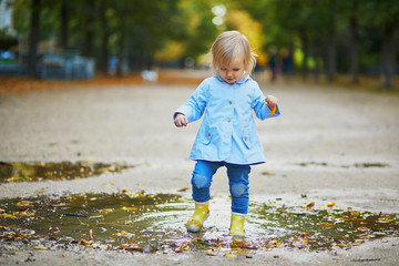Child wearing yellow rain boots and jumping in puddle