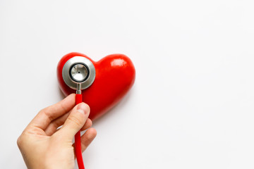 Fototapeta na wymiar Closeup of man hand holding a red stethoscope on heart - medical diagnostic device for auscultation (listening) of sounds coming from the heart, bronchi, isolated, blurred heart on white background. 