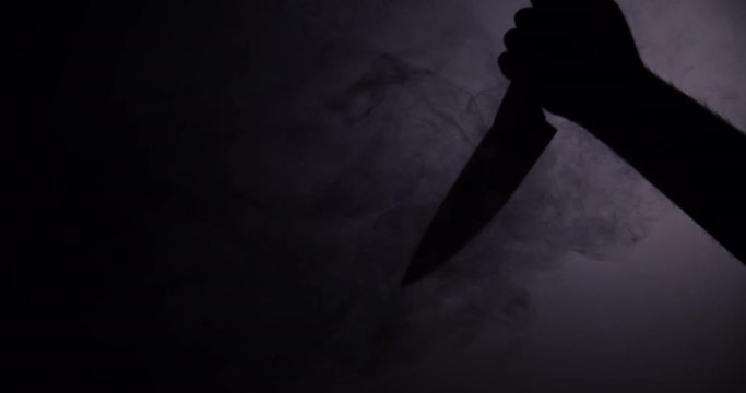 Shadow of killer hand raising knife to stab with black smoke. Dark silhouette.