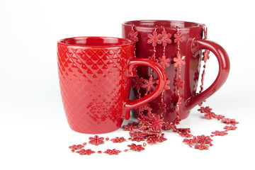 Two red ceramic cups with a garland on a white background..Red Christmas garland in a mug.