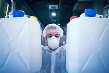 Technologist industrial worker in protective suit holding plastic canisters with chemicals in...