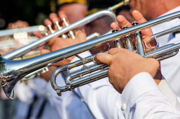 Hands of a man holding a trumpet musical instrument, a military band plays music
