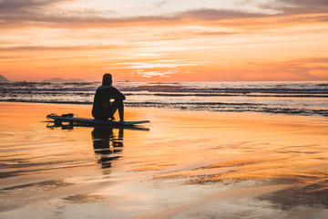 Silhouette of a surfer sitting on the beach of the Atlantic Ocean, near San Sebastian and Bilbao, North of Spain, Europe watching a dramatic stunning colorful sunset