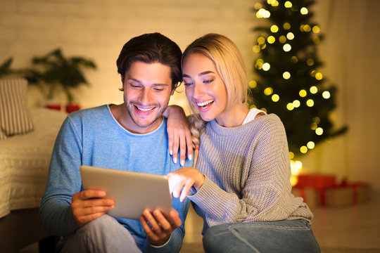 Couple looking at old photos on tablet next to Christmas tree
