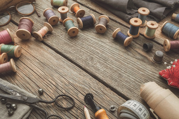 Vintage sewing items: retro tailoring scissors, measuring tape, thimble, wooden spools of thread, patterns on paper, cutting knife, cushion for including pins, needles. Top view. Copy space for text.