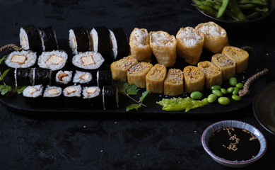 Vegan maki, inari sushi, tamagoyaki, edamame on black background