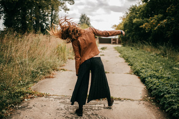Portrait from behind of strange stylish woman walking like zombie on the road at nature