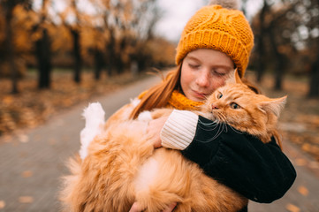 Beautiful freckles girl holding her loving kitten in a valley of autumn park.
