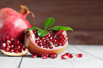 Fresh ripe juicy whole and split pomegranate fruit with leaves on rustic background, healthy red...