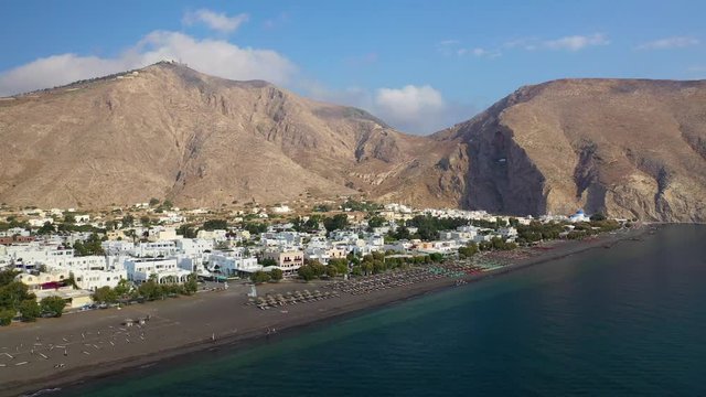 Aerial drone video of famous organised with umbrellas and sunbeds black sand beach and bay of Perissa village, Santorini island, Cyclades, Greece