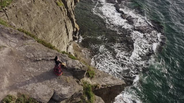 Top aerial view of sensual gipsy woman with guitar on high cliff enjoying ocean fresh wind on her face and skin