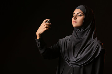 Beautiful Muslim woman with perfume on dark background