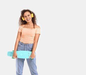 Beautiful African-American woman with skateboard listening to music on white background