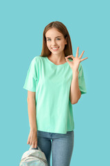 Beautiful female student showing OK on color background