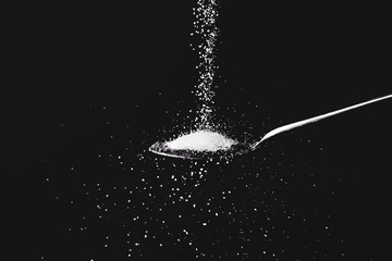 Sprinkling of sugar into spoon with tasty jam against dark background