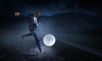 Fototapeta na wymiar Black businessman plays football with Moon