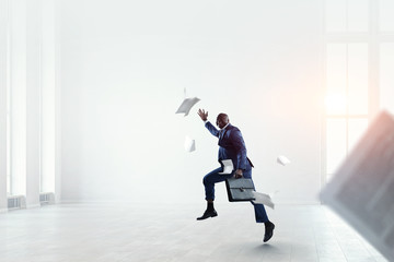 Black businessman with briefcase running among flying papers indoor