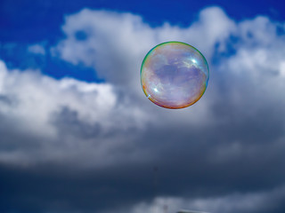 One colorful soap bubble flying front of the cloudy blue sky