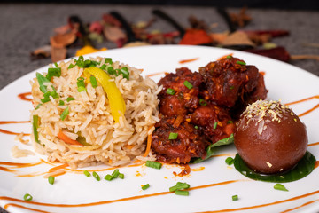 Fried rice with chili chicken and a gulab jamun for Indian lunch menu. Garnished with spices and green onion. Extra copy space for text.