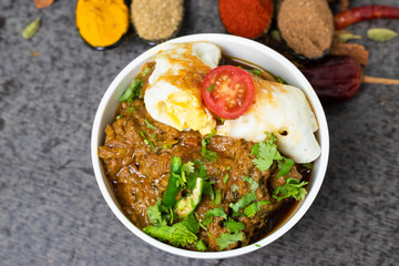 Chicken curry with egg omelet in a white bowl garnished with Indian spices and red tomato. Extra copy space for text.