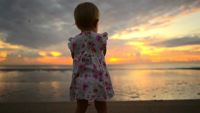 Little pretty girl in white dress dancing on the beach. Beautiful sunny morning at the sea. Stylish baby girl