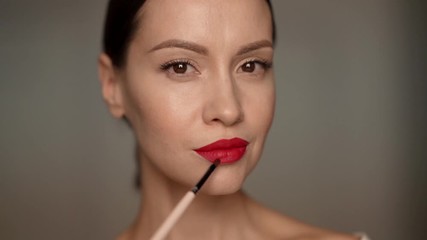 Closeup portrait of beautiful woman applying makeup with brush. Young attractive confident brunette lady on white background. Female natural beauty. Slow motion video - Powered by Adobe