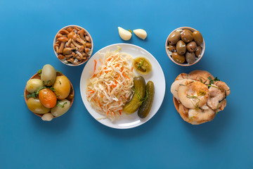 Fermented products cabbage, peppers, pickles, tomatoes, mushrooms, zucchini, garlic on a blue table. Top view. Copy space