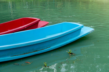 Red and blue plastic boat on the beautiful green water surface.
