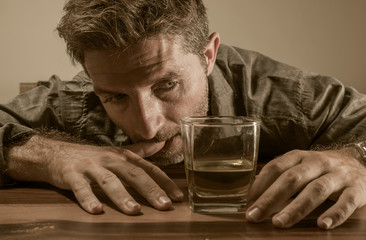 alcoholic depressed and drunk addict man sitting in front of whiskey glass trying holding on drinking in dramatic expression suffering alcoholism and alcohol addiction