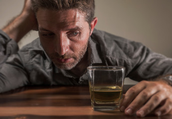 alcoholic depressed and drunk addict man sitting in front of whiskey glass trying holding on drinking in dramatic expression suffering alcoholism and alcohol addiction