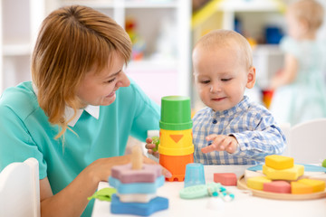 Nursery child boy playing toys with teacher in classroom in kindergarten