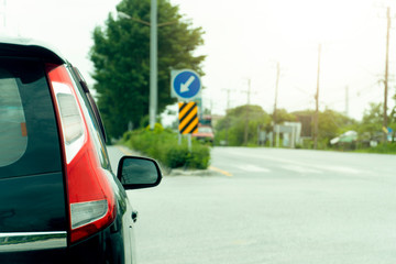 The rear view of the luxurious black car is parked on an empty street intersection. On the opposite side there are trees and a blurry U-turn signal.