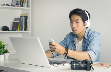 Asian Freelance Videographer Checking Multimedia File by Smartphone with Laptop in Home Office in Vintage Tone