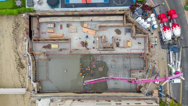 Aerial time lapse of a concrete pour crane on a construction development site with workers below building a house foundation