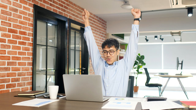 Young asian businessman arms up with happiness while looking at laptop computer at office, Asia office man celebration after success job, people office lifestyle