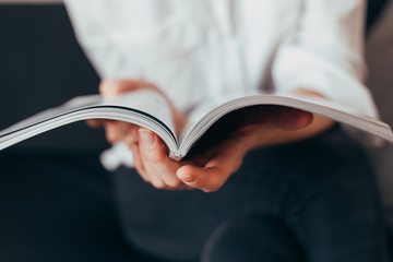 Beautiful female hands hold an open book or magazine in the room
