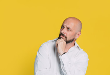 Handsome serious middle aged man meditate on yellow background with copy space.