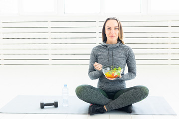 sport, healthy, people concept - Girl holding salad and dumbbell after fitness training