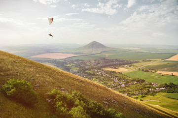 A paraglider flies in the sky in a cocoon suit on a paraglider over the Caucasian countryside with...