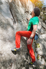 A free aged male climber hangs on a rock wall in a forest in the mountains. Mature Sports Concept