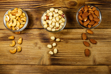 Assortment of nuts on wooden table. Almond, hazelnut and cashew in glass bowls. Top view. Healthy eating concept