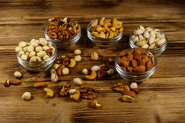 Assortment of nuts on wooden table. Almond, hazelnut, pistachio, walnut and cashew in glass bowls. Healthy eating concept