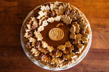 Homemade Pumpkin Pie Decorated with Pastry Cutouts of Autumn leaves with a center pumpkin, set on a wooden board with fresh pumpkins and pecans, selective focus